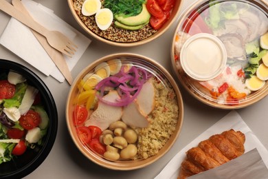 Photo of Tasty food in containers with wooden knife and fork on light grey table, flat lay