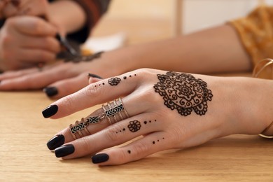 Photo of Professional mehndi master making henna tattoo at table, closeup