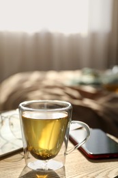 Photo of Glass cup of freshly brewed tea on wooden table in bedroom. Cozy home atmosphere