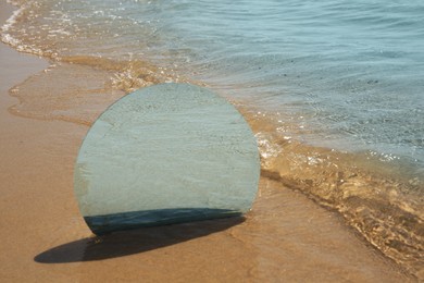 Round mirror reflecting sea on sandy beach. Space for text