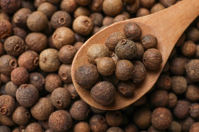 Photo of Aromatic allspice pepper grains and wooden spoon, top view