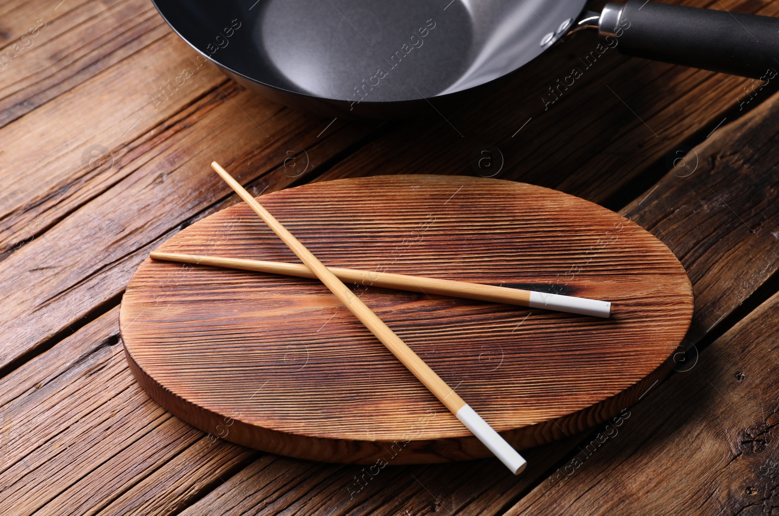 Photo of Serving board with chopsticks and iron wok on wooden table, closeup