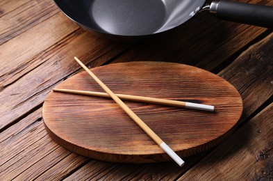 Serving board with chopsticks and iron wok on wooden table, closeup