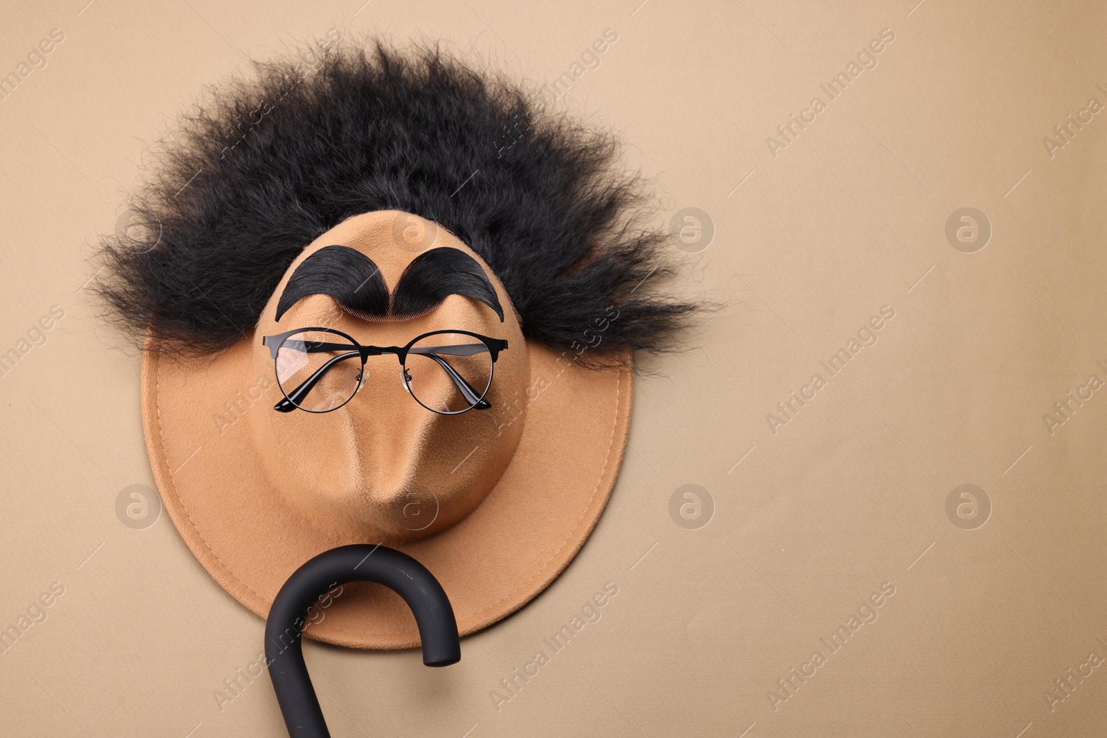 Photo of Man's face made of artificial hair, eyebrows, glasses and hat on beige background, top view. Space for text