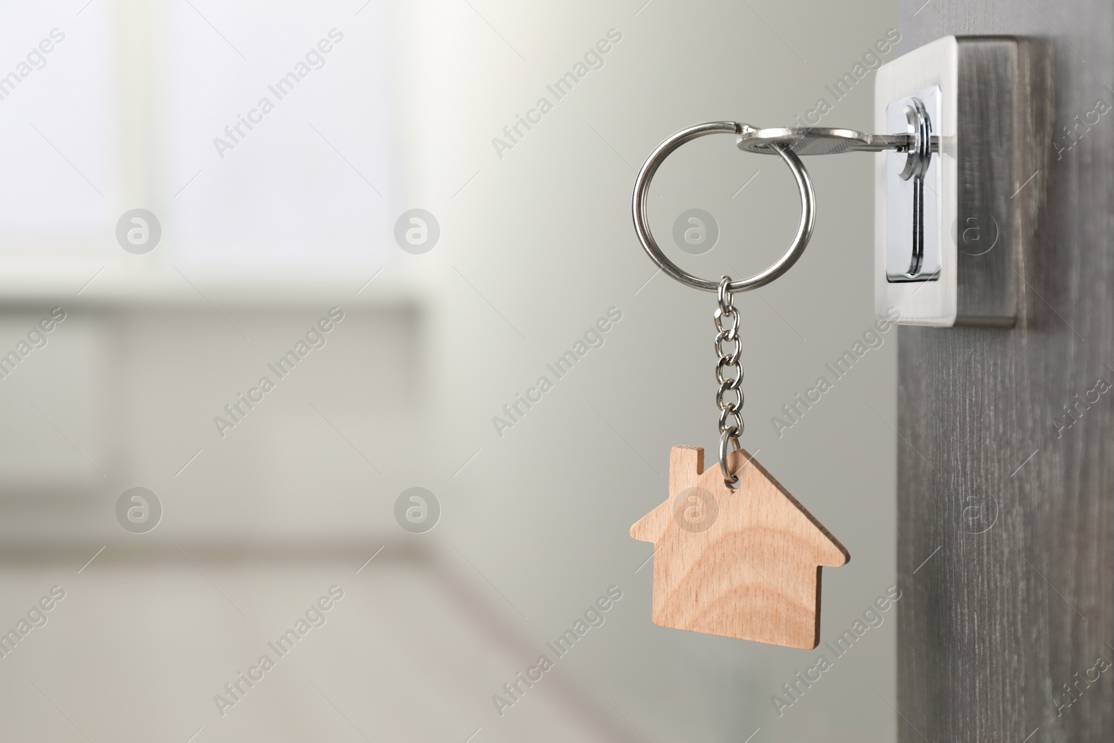 Photo of Mortgage and real estate. Open door with key and house shaped keychain against blurred background, space for text