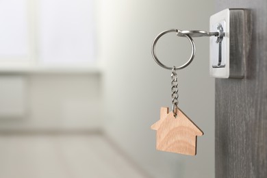 Photo of Mortgage and real estate. Open door with key and house shaped keychain against blurred background, space for text