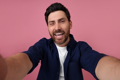 Photo of Smiling man taking selfie and winking on pink background