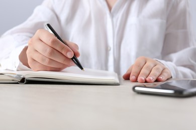 Woman writing in notebook at wooden table in office, closeup