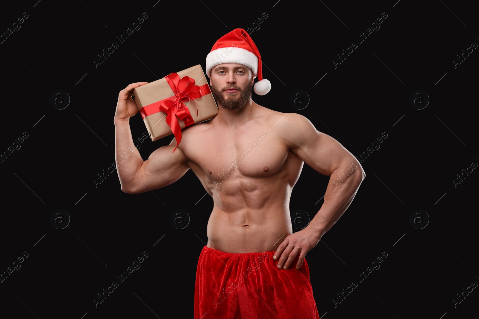 Photo of Attractive young man with muscular body holding Christmas gift box on black background