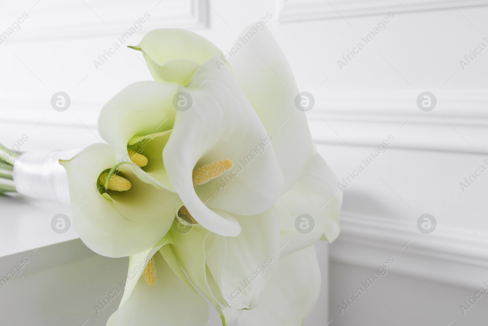 Photo of Beautiful calla lily flowers tied with ribbon on white table, closeup