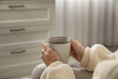 Woman with cup of hot drink resting at home, closeup
