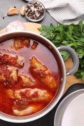 Photo of Delicious stuffed cabbage rolls cooked with homemade tomato sauce in pot and ingredients on grey table, flat lay