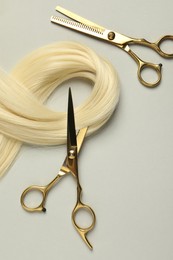 Professional hairdresser scissors with blonde hair strand on light grey background, flat lay