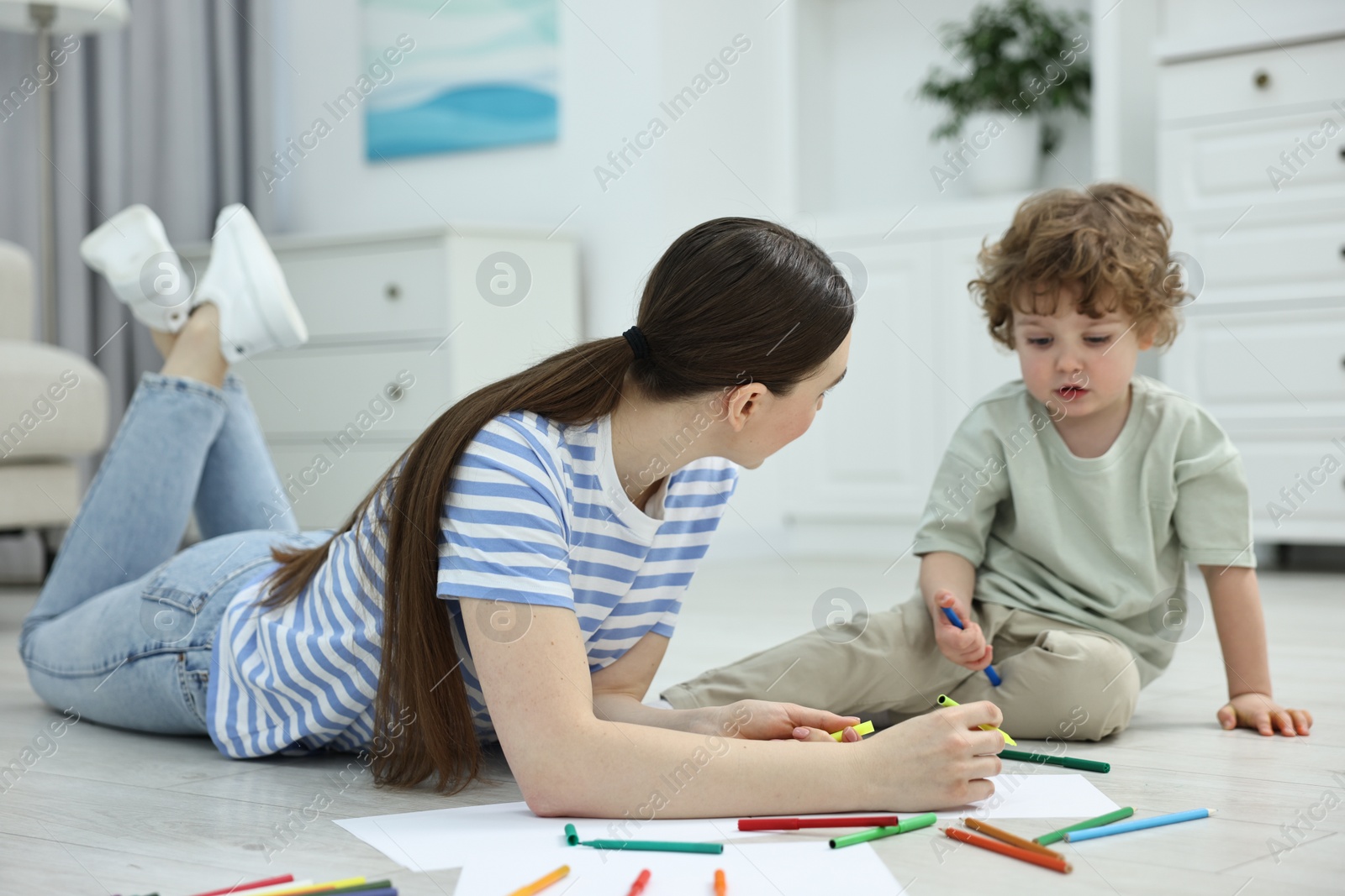 Photo of Mother and her little son drawing with colorful markers on floor at home