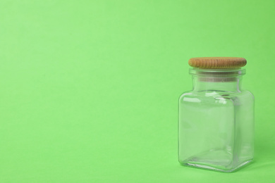 Photo of Closed empty glass jar on light green background, space for text