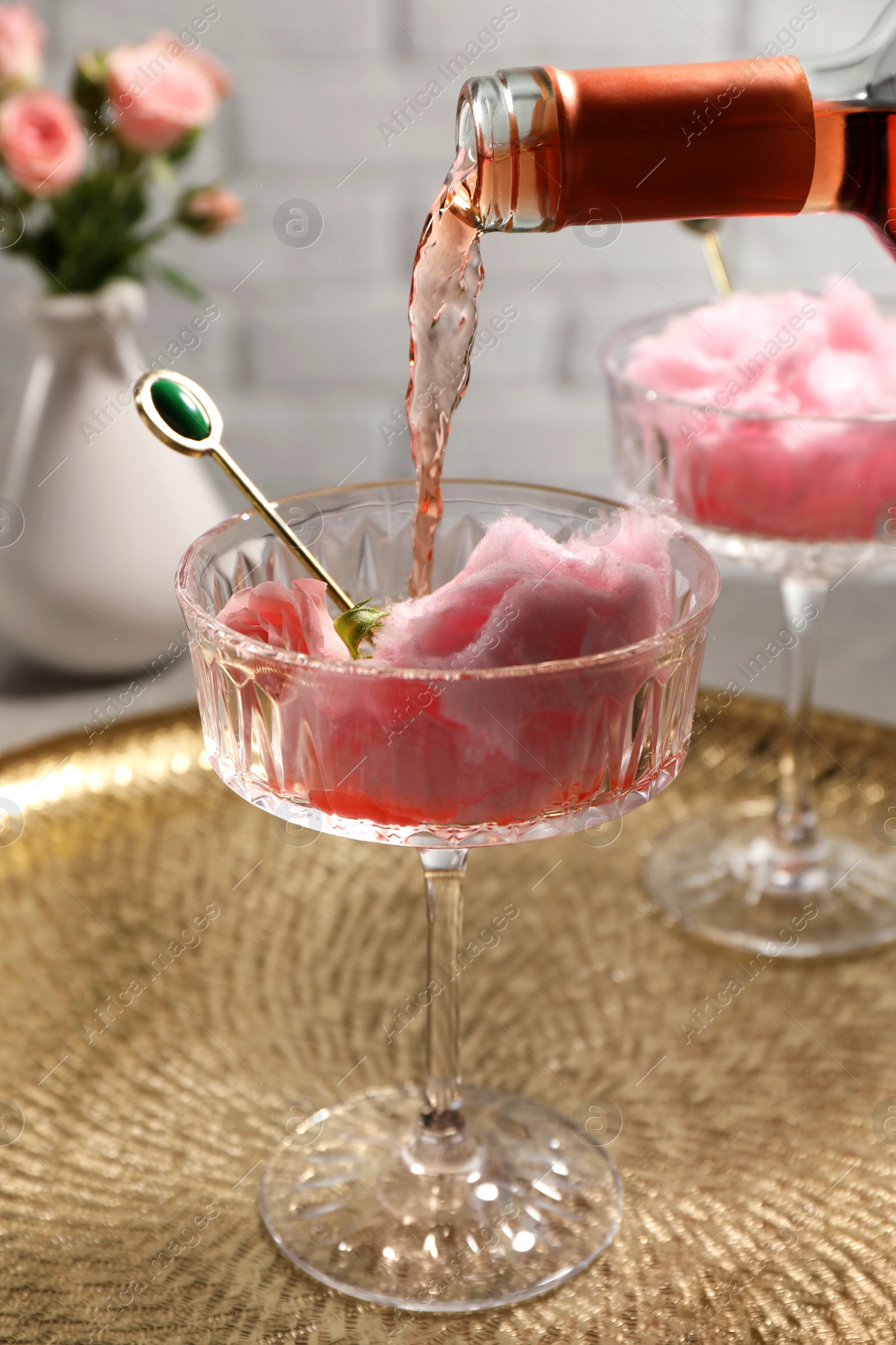 Photo of Pouring rose wine from bottle into glass with cotton candy on golden tray