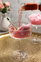 Photo of Pouring rose wine from bottle into glass with cotton candy on golden tray