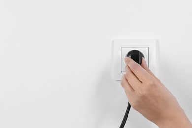 Woman putting plug into power socket on white background, closeup. Electrician's equipment