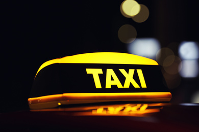 Photo of Taxi car with yellow roof sign on city street at night, closeup