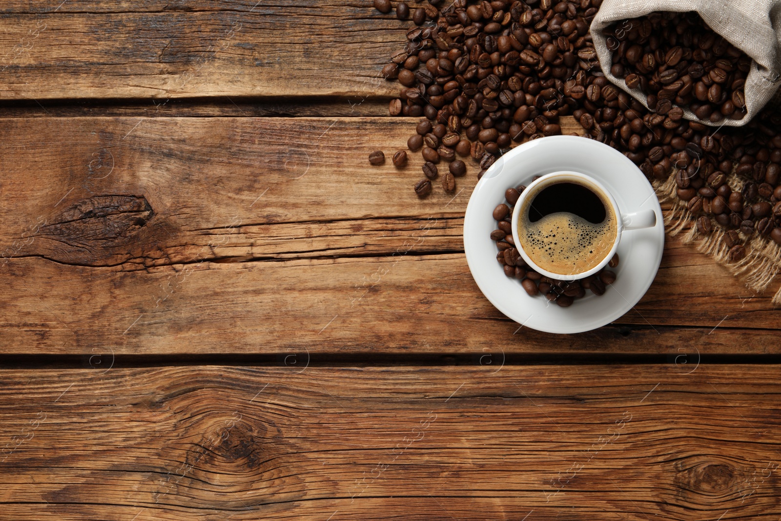 Photo of Cup of aromatic hot coffee and beans on wooden table, flat lay. Space for text