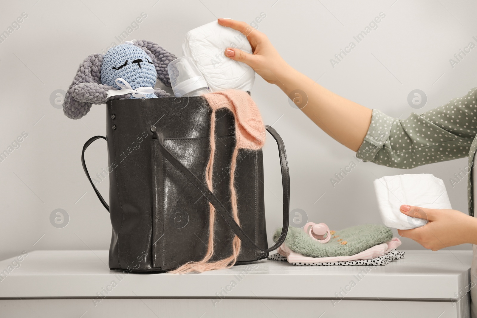 Photo of Woman putting diaper into mother`s bag at white table indoors, closeup