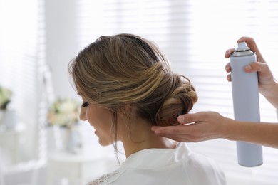 Photo of Professional stylist using hair spray while working with bride before her wedding, back view