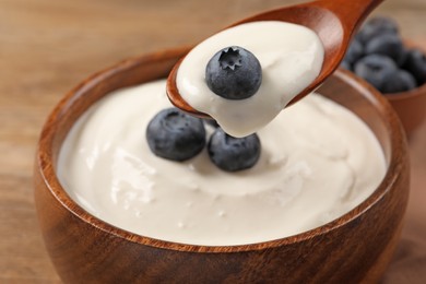 Eating tasty yogurt with blueberries from bowl on wooden table, closeup