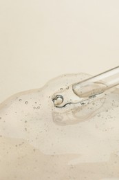 Photo of Dripping cosmetic oil from pipette onto beige background, closeup. Space for text