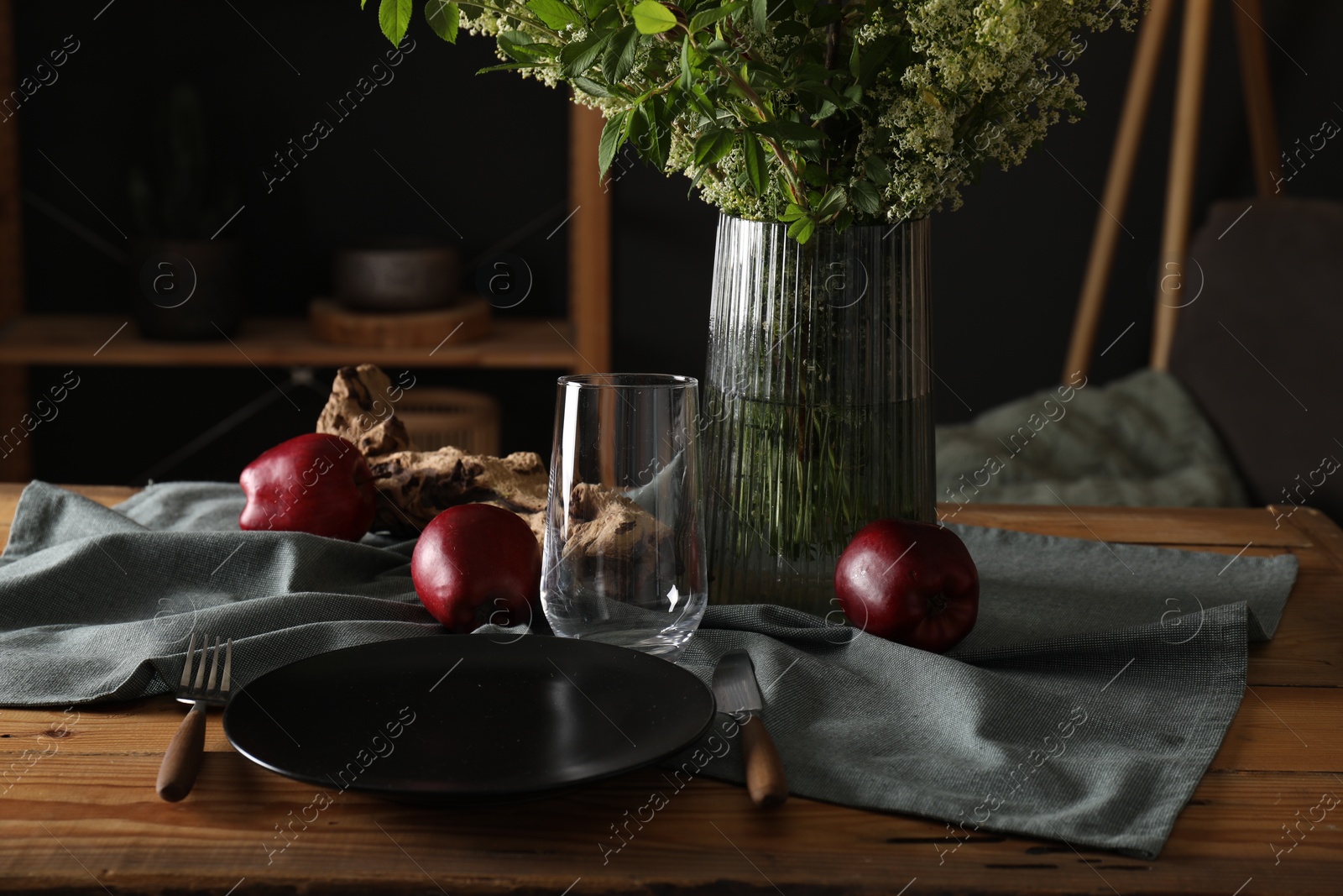 Photo of Set of clean dishware, ripe red apples and flowers on dining table indoors