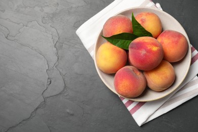 Fresh peaches and leaves in bowl on grey textured table, top view. Space for text