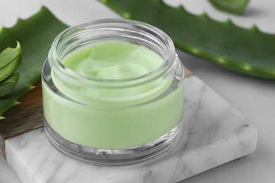 Photo of Jar with cream and cut aloe leaves on white table, closeup
