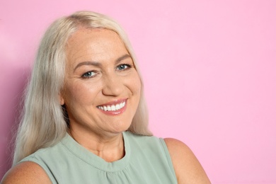 Portrait of mature woman with beautiful face on pink background. Space for text