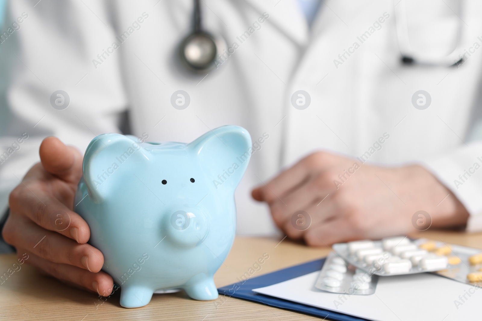 Photo of Doctor with piggy bank at wooden table, closeup