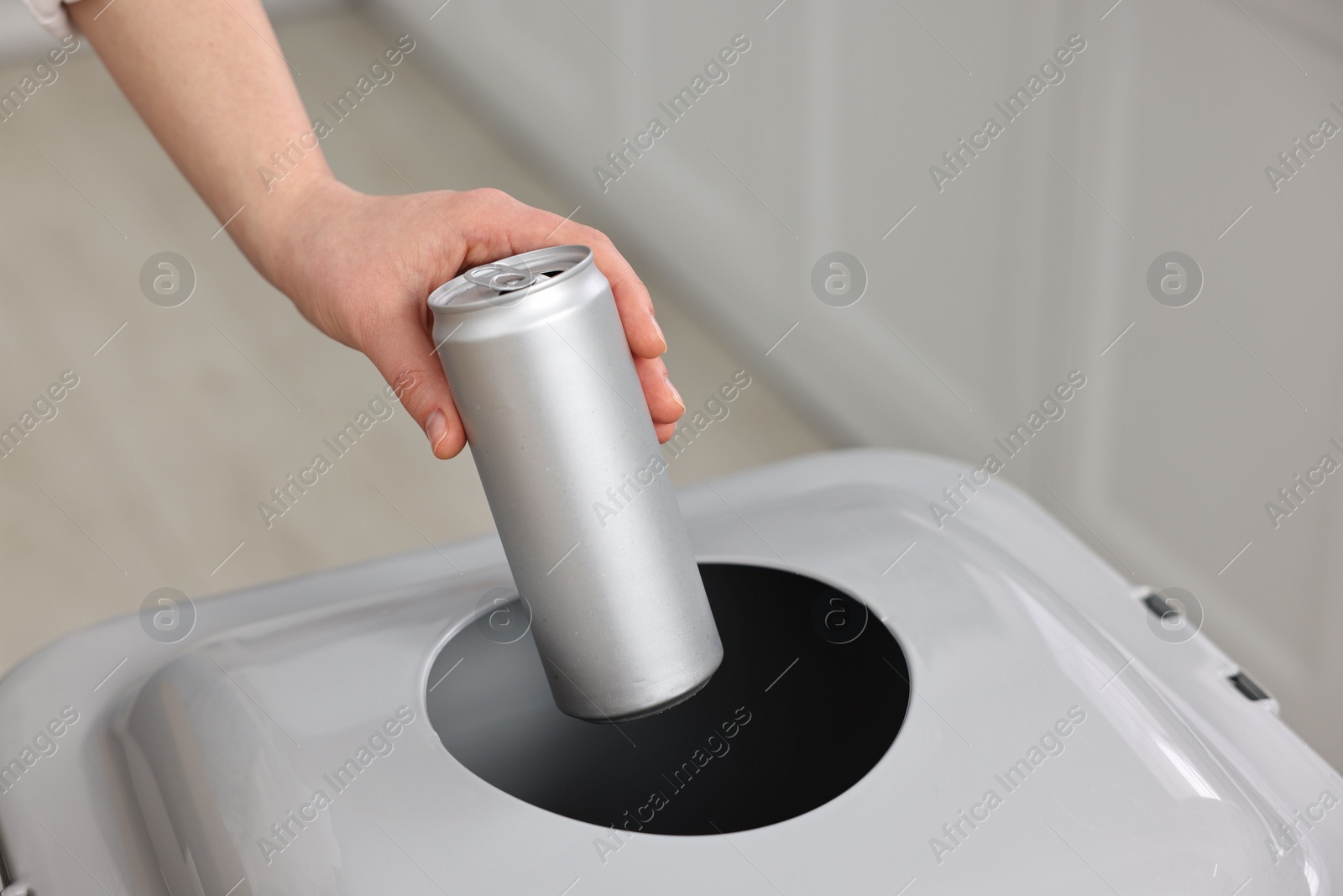 Photo of Garbage sorting. Woman throwing metal can into trash bin indoors, closeup