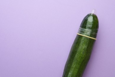 Photo of Cucumber with condom on lilac background, top view and space for text. Safe sex concept