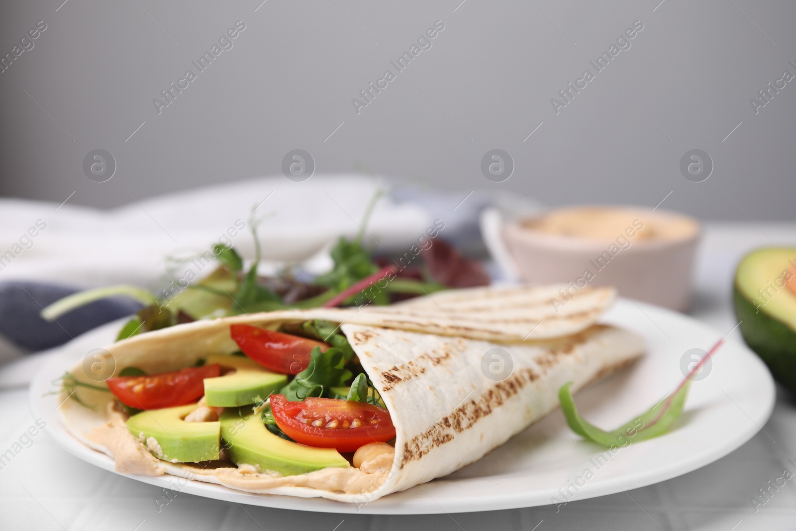 Photo of Plate with hummus wrap and vegetables on table, closeup. Space for text