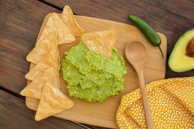 Photo of Delicious guacamole made of avocados, nachos and spoon on wooden table, flat lay