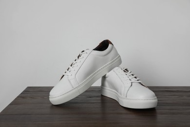 Photo of Pair of stylish white sneakers on wooden table against light background