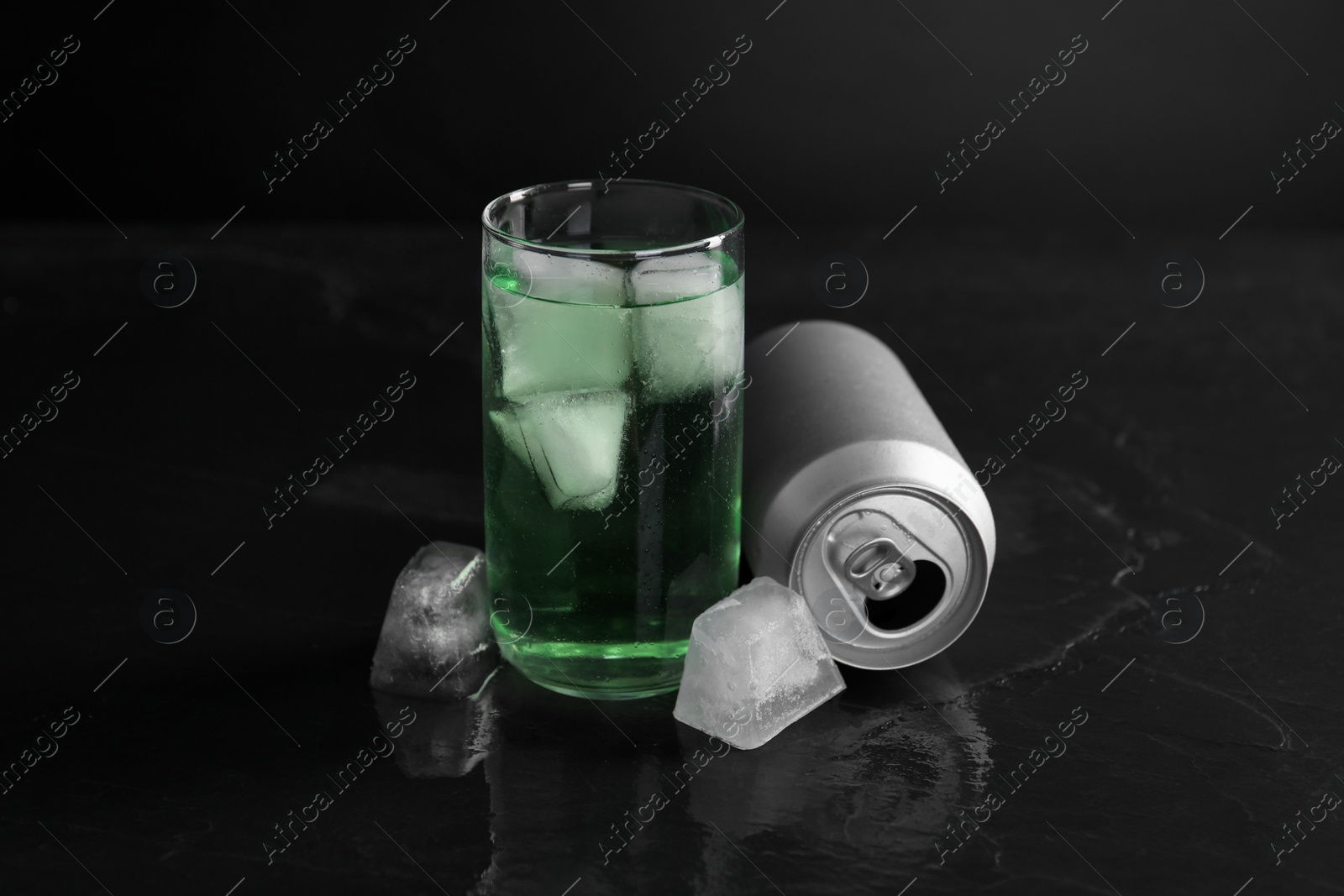 Photo of Tasty energy drink with ice cubes in glass and aluminium can on black table