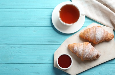 Photo of Marble board with tasty croissants, cup of tea and space for text on light blue wooden background, flat lay. French pastry