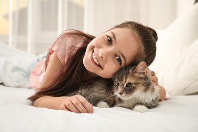 Cute little girl with cat lying on bed at home. First pet