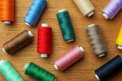 Photo of Many colorful sewing threads on wooden table, flat lay