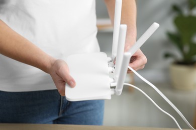 Photo of Woman connecting cable to Wi-Fi router at table indoors, closeup