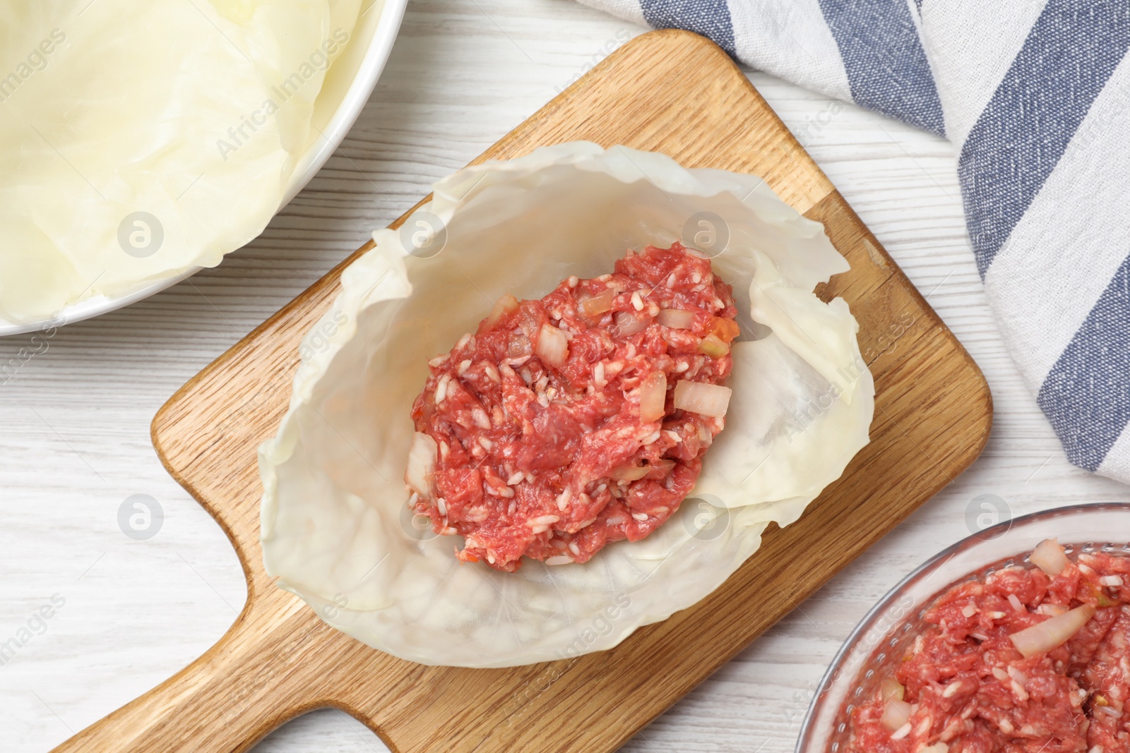 Photo of Preparing stuffed cabbage roll on white wooden table, flat lay