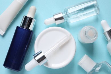 Photo of Many bottles and tube of cosmetic serum on light blue background, flat lay