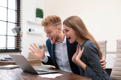 Happy young people playing online lottery using laptop in office