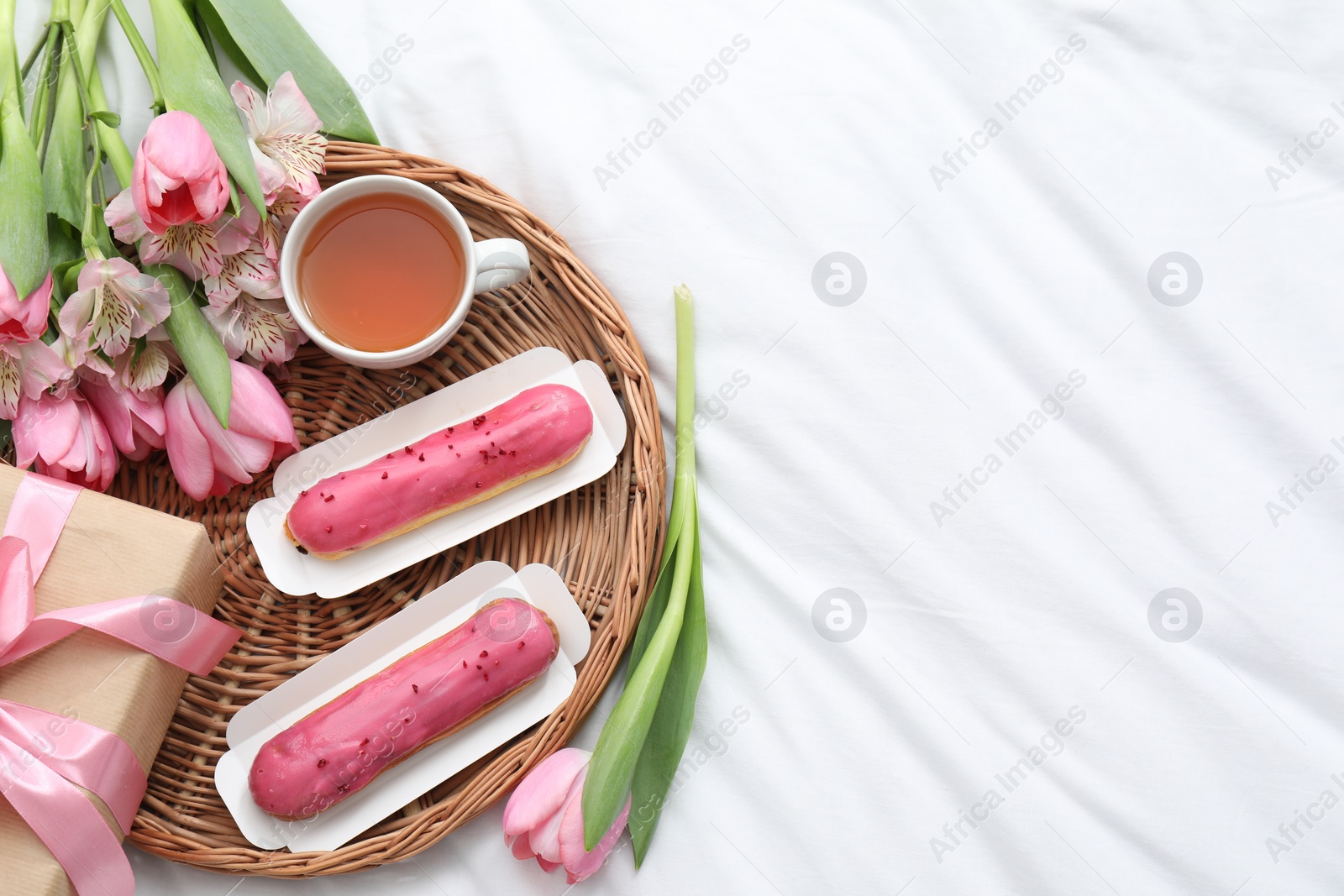 Photo of Tasty breakfast. Delicious eclairs, tea, flowers and gift box on bed, top view. Space for text