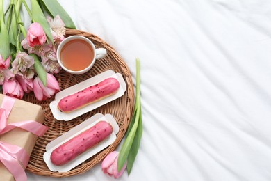 Photo of Tasty breakfast. Delicious eclairs, tea, flowers and gift box on bed, top view. Space for text