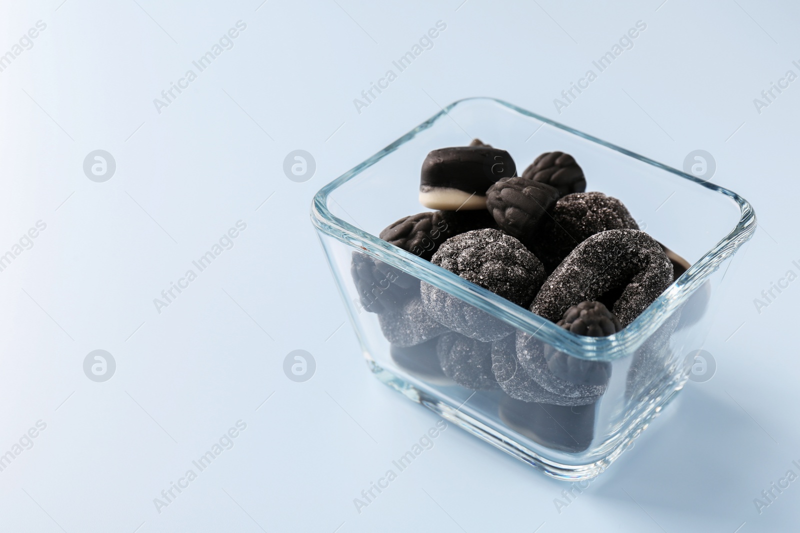 Photo of Glass container of tasty liquorice candies on light blue background, space for text