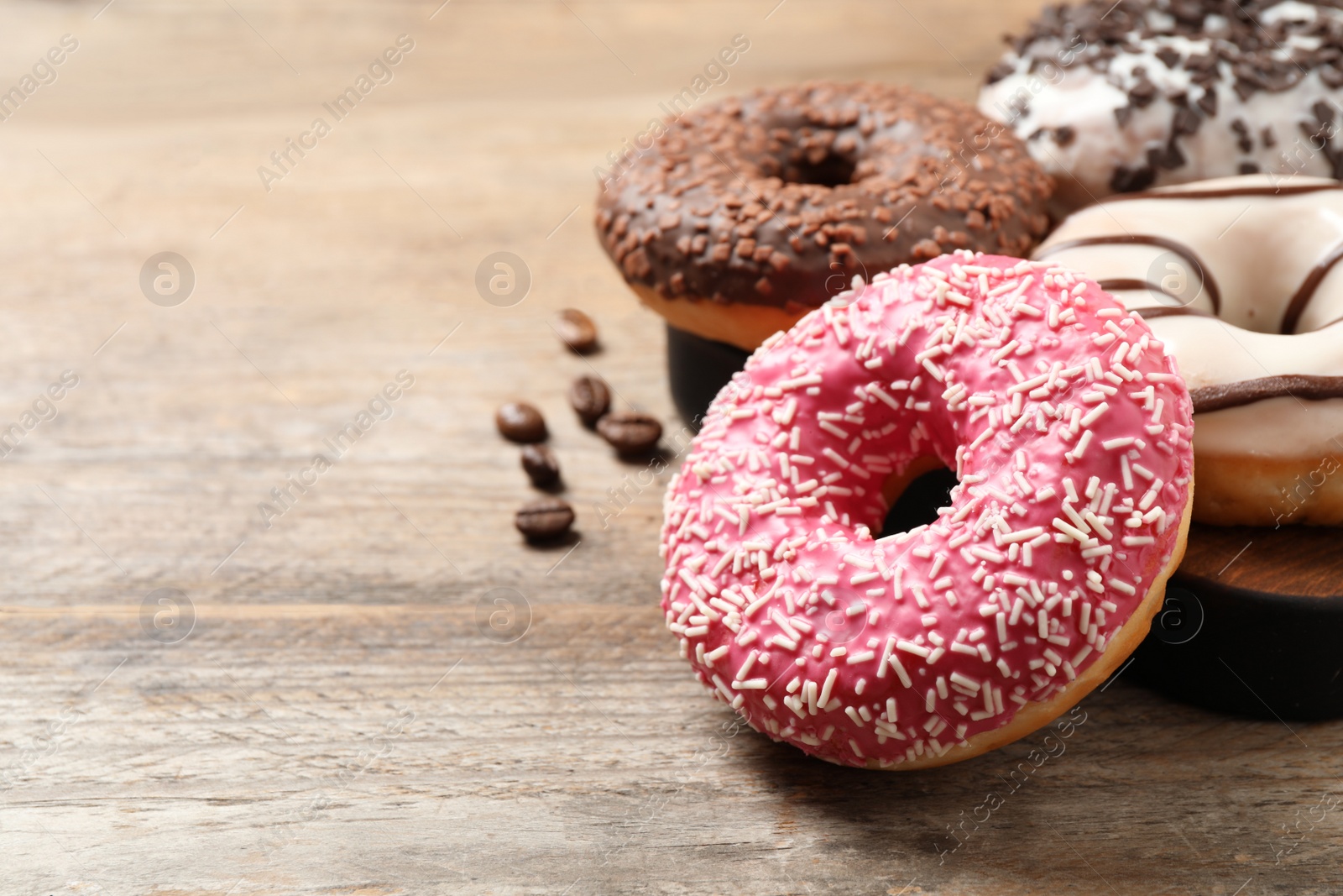 Photo of Yummy donuts with sprinkles on wooden table, closeup. Space for text